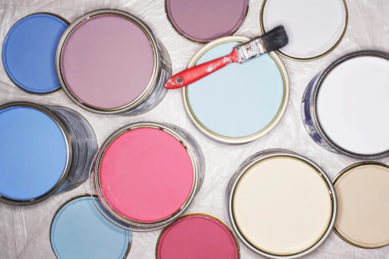 Various open paint cans with pastel and vibrant colors and a paintbrush.